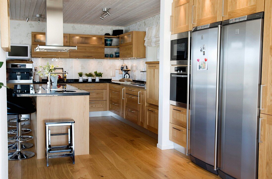 Geräumige offene Küche mit Holzfronten und Parkettboden, an der Küchentheke moderne schwarze Barhocker mit Edelstahlfuß