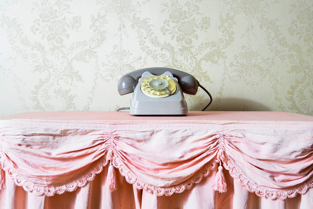 Stillleben mit grauem Vintage-Telefon auf rosafarbener Rüschentischdecke