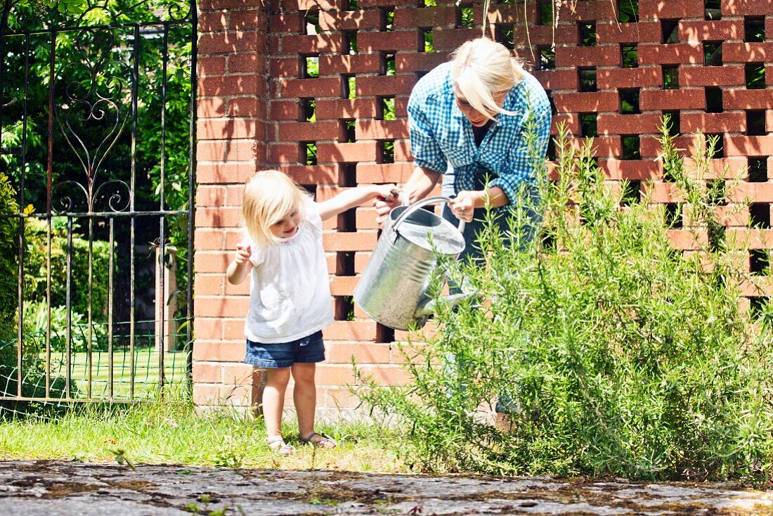 Mutter mit kleiner Tochter beim Gießen im Garten mit hoher Ziegel Gartenmauer