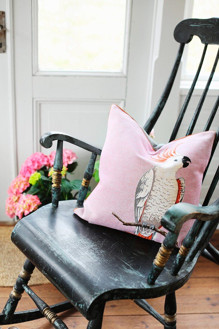 Nostalgischer Holzschaukelstuhl mit rosafarbenem Dekokissen in nordischem Landhausambiente