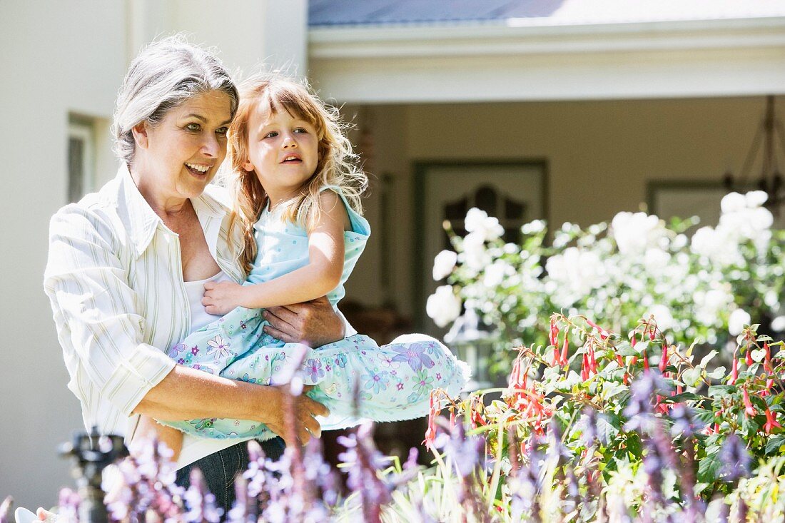 Grossmutter mit Enkelin auf dem Arm beim Betrachten der Blumen im Garten