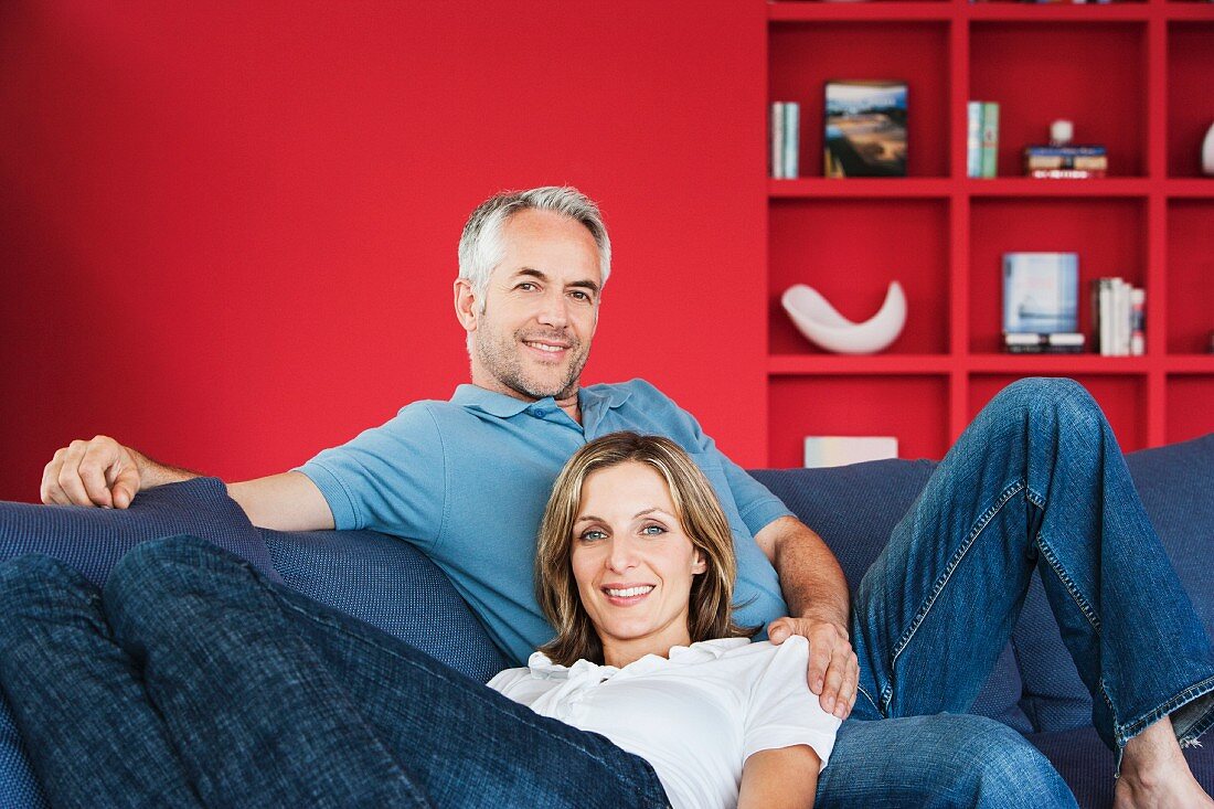 Ein Paar beim Entspannen auf dem Sofa; im Hintergrund eine rote Wand mit Einbauregal