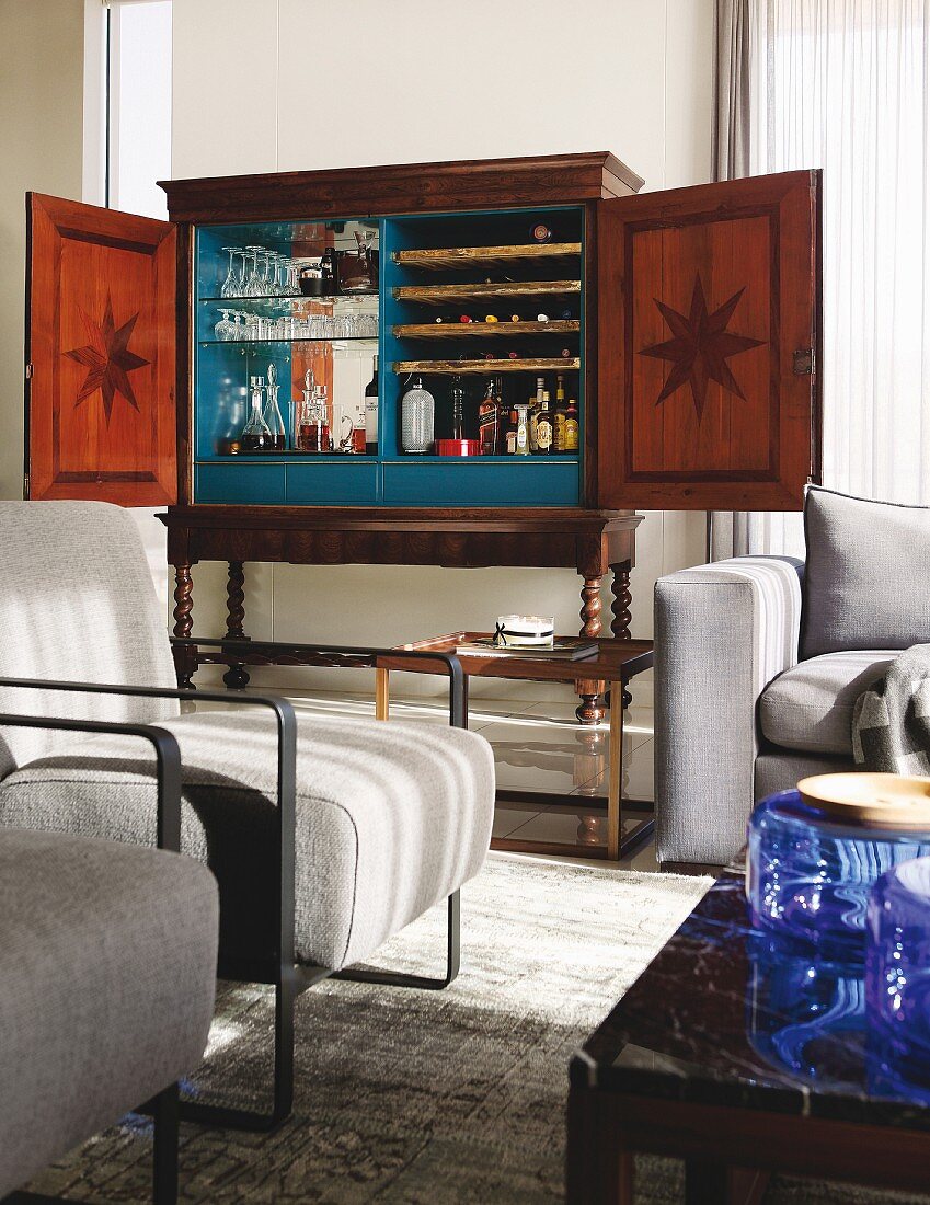 Minibar in antique walnut cabinet in lounge area with pale armchairs