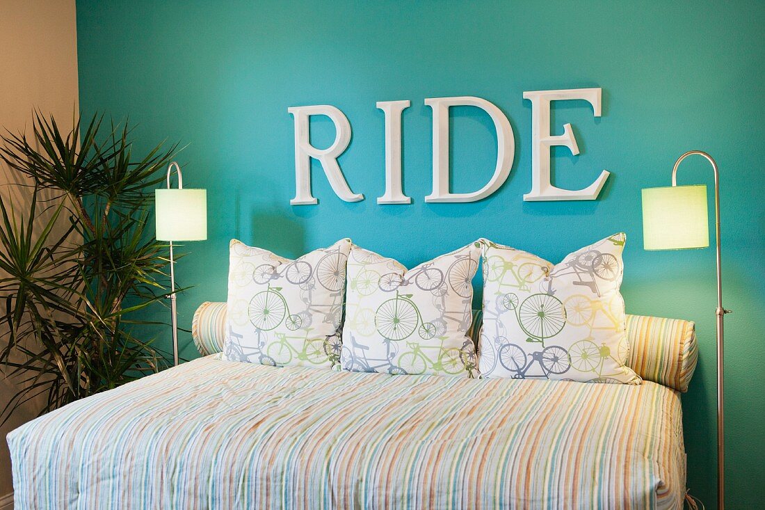 Schlafzimmer mit Schriftzug Ride an blauer Wand über Doppelbett mit Fahrradmotiven auf der Bettwäsche