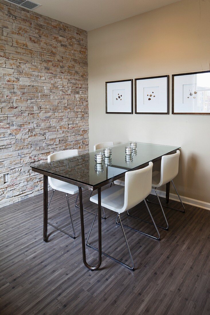 Esstisch aus Glas mit Freischwinger Stühlen in schlichtem Wohnraum mit Steinwand & Holzfussboden