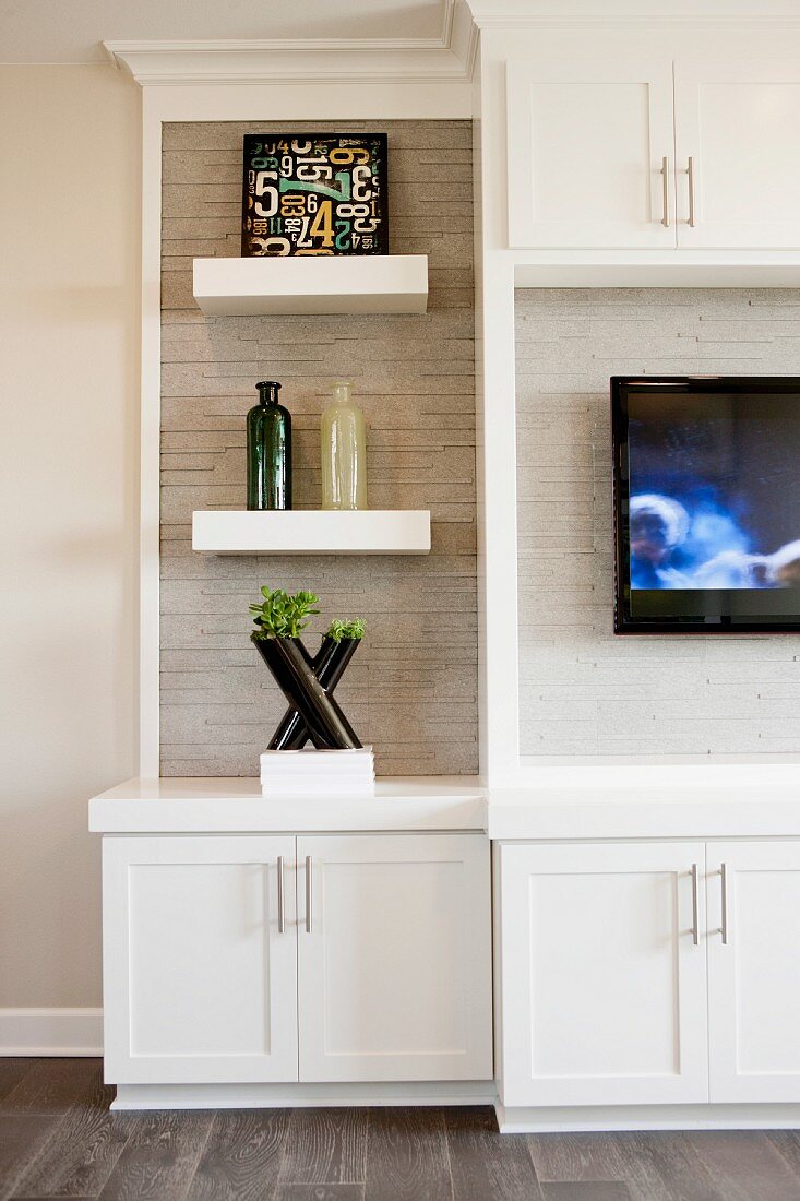weiße Wohnzimmerschrankwand mit TV-Gerät & Dekoobjekten auf Konsolenbrettern