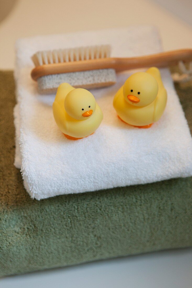 Zwei Gummi-Enten und eine Massagebürste auf Stapel Duschhandtüchern