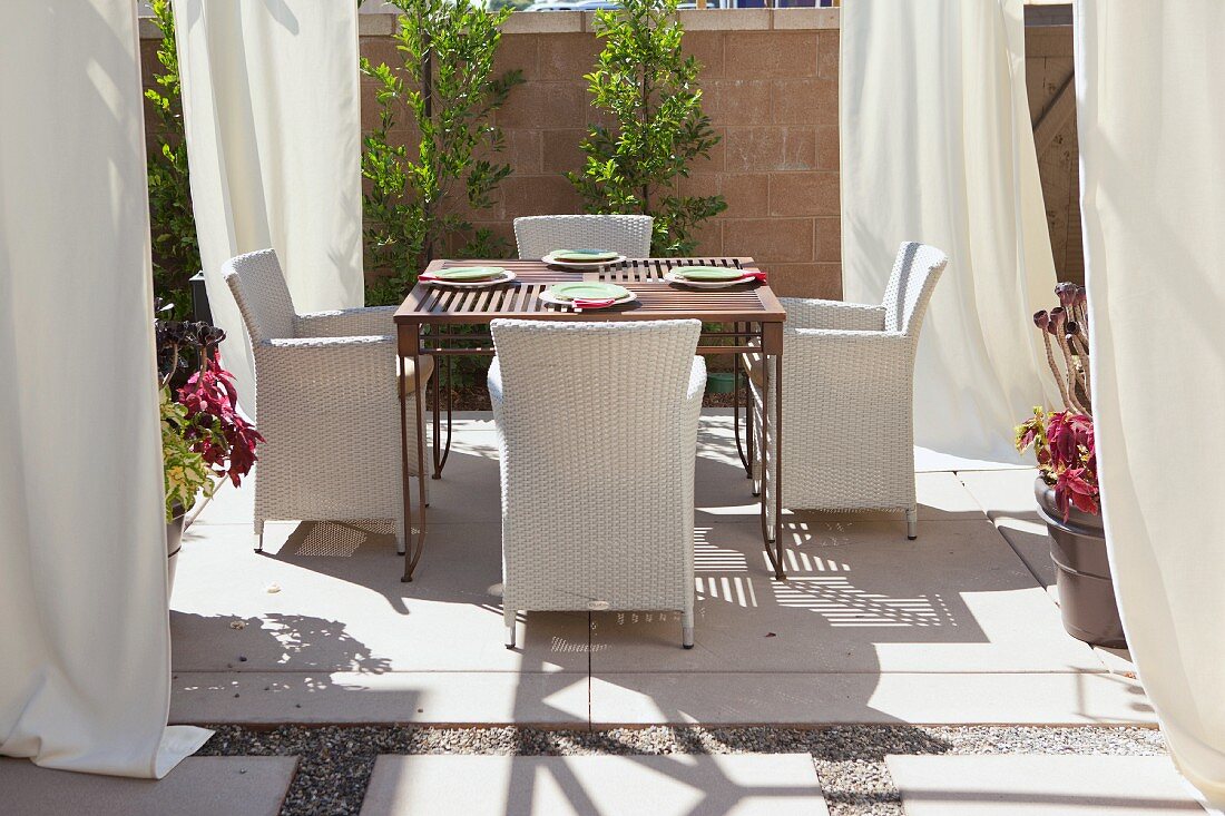 Esstisch mit Outdoorsesseln auf Terrasse mit weissen Vorhängen als Deko & Sonnenschutz