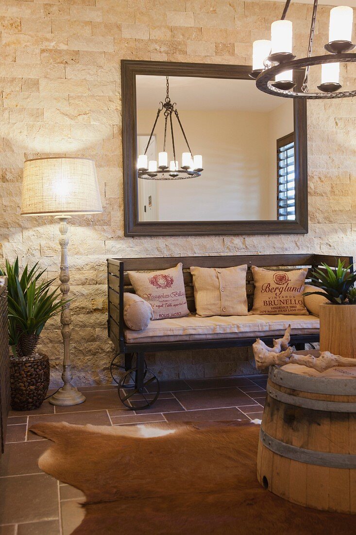 Rustikaler Wohnraum mit rollbarer Sitzbank, Tierfellteppich, Holzfass als Couchtisch & Wandspiegel an gemauerter Zimmerwand