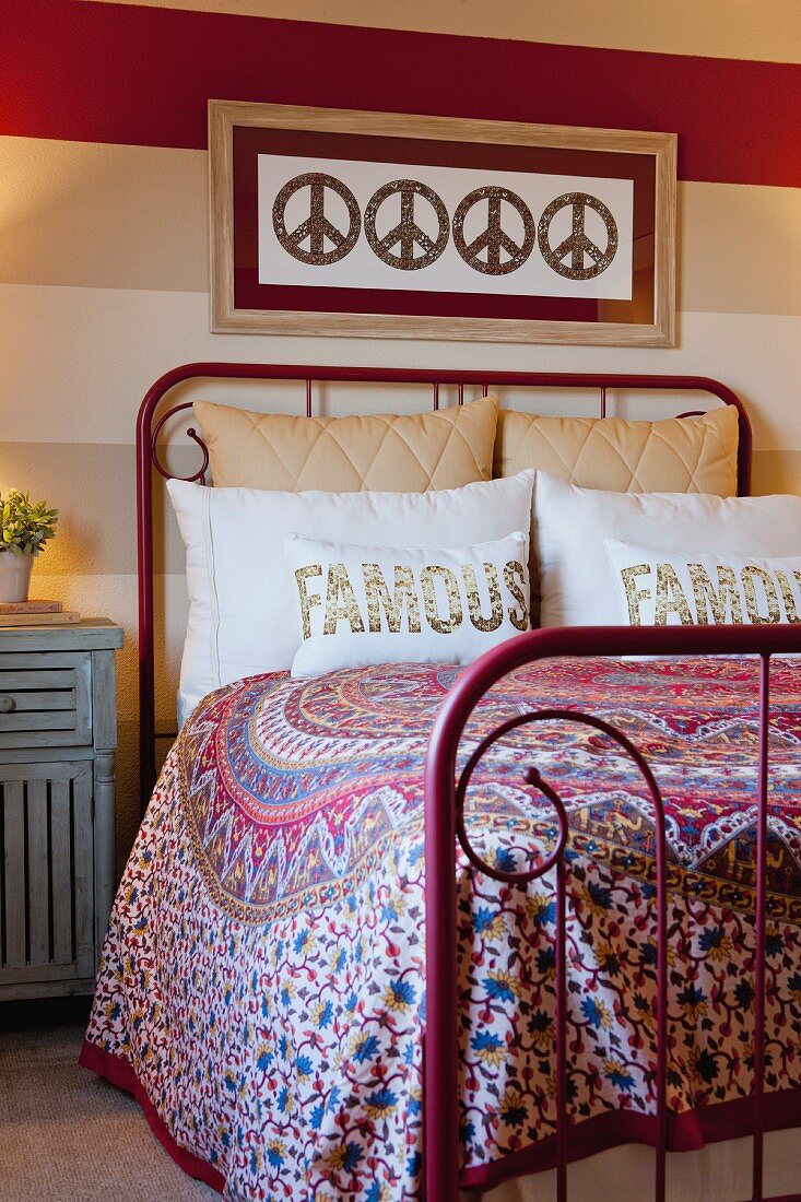 Rotes schmiedeeisernes Bett mit bunter Tagesdecke und Zierkissen