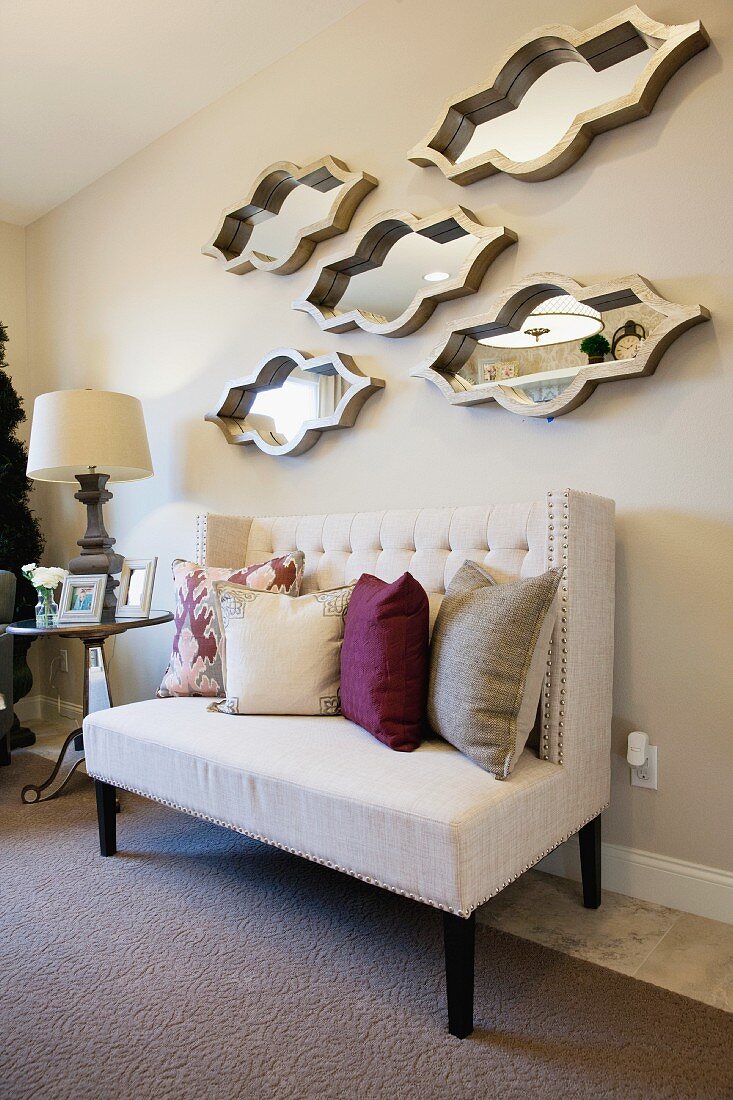 Wohnraum mit weißem Sofa, Zierkissen, Beistelltisch & dekorativen Spiegelobjekten als Wanddekoration