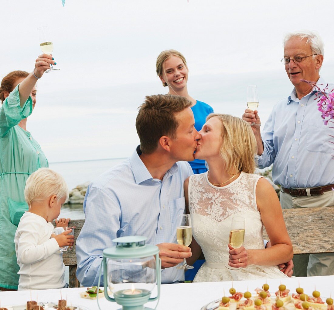 Paar mittleren Alters mit Sektgläsern küssen sich auf Hochzeitsfeier