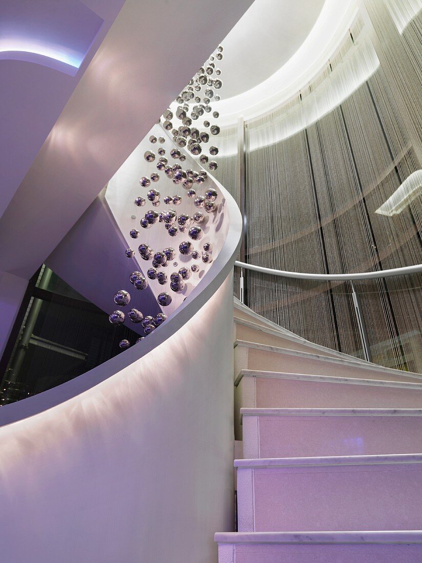 Beleuchtete Wendeltreppe eines Luxus-Hotels mit Fadenvorhängen & Dekoobjekt aus Kugeln