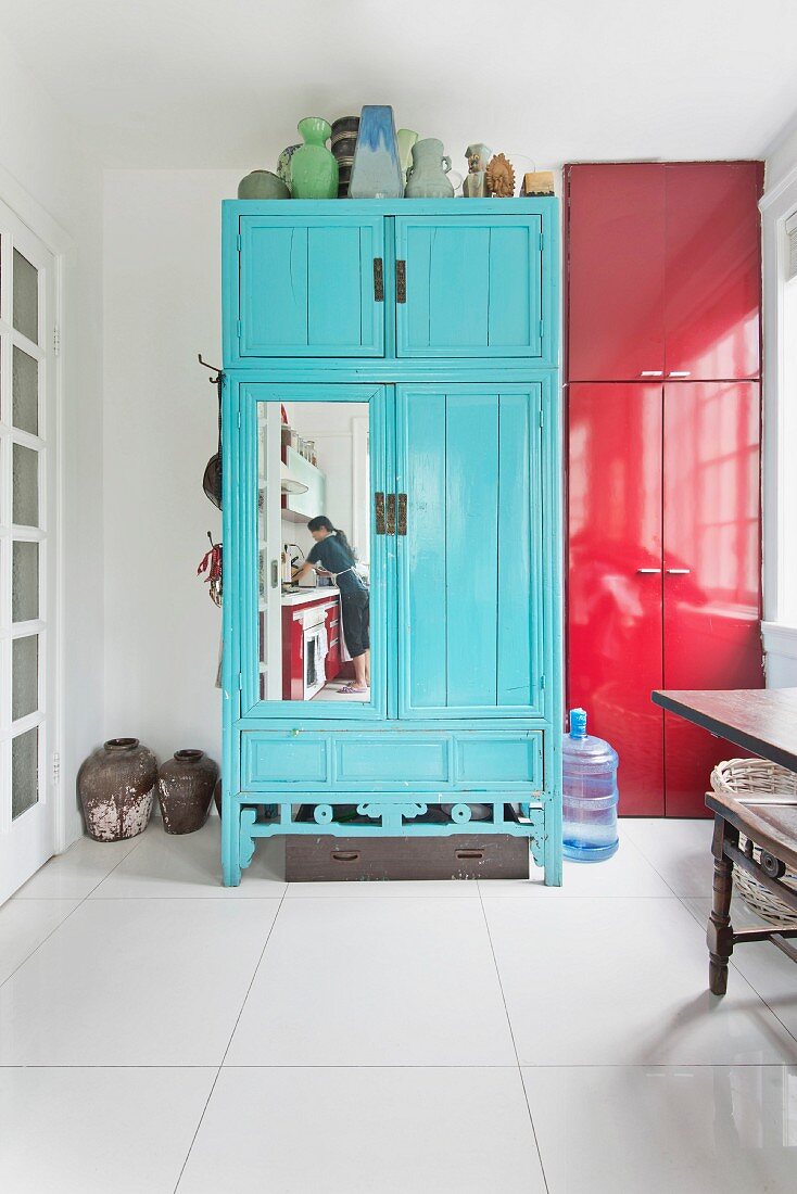 Reflection of woman washing dishes in kitchen in mirror on blue cupboard door