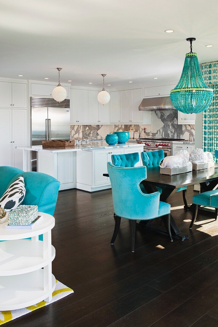 Offener Wohnraum in Weiß mit blauen Farbakzenten, dunklem Dielenboden, Esstisch & Küche im Hintergrund