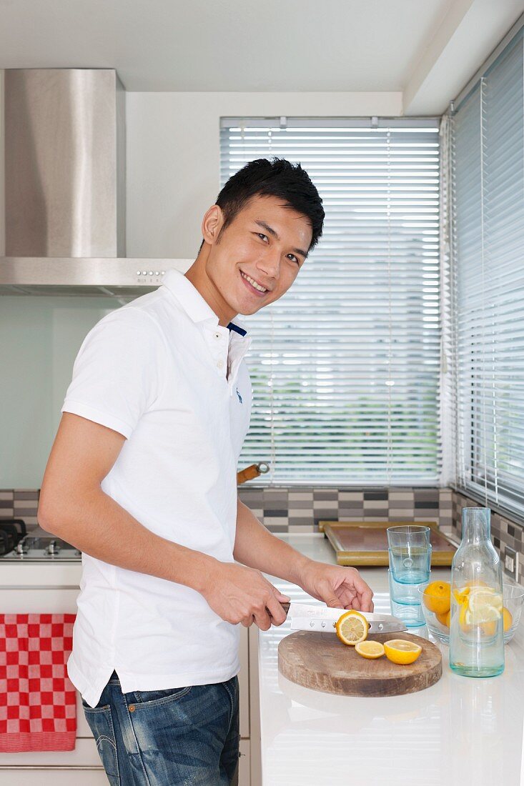 Lächelnder junger Mann schneidet Zitronen in der Küche