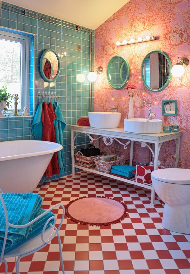Bathroom with free-standing bathtub on red and white chequered floor and twin basin on ornate metal washstand