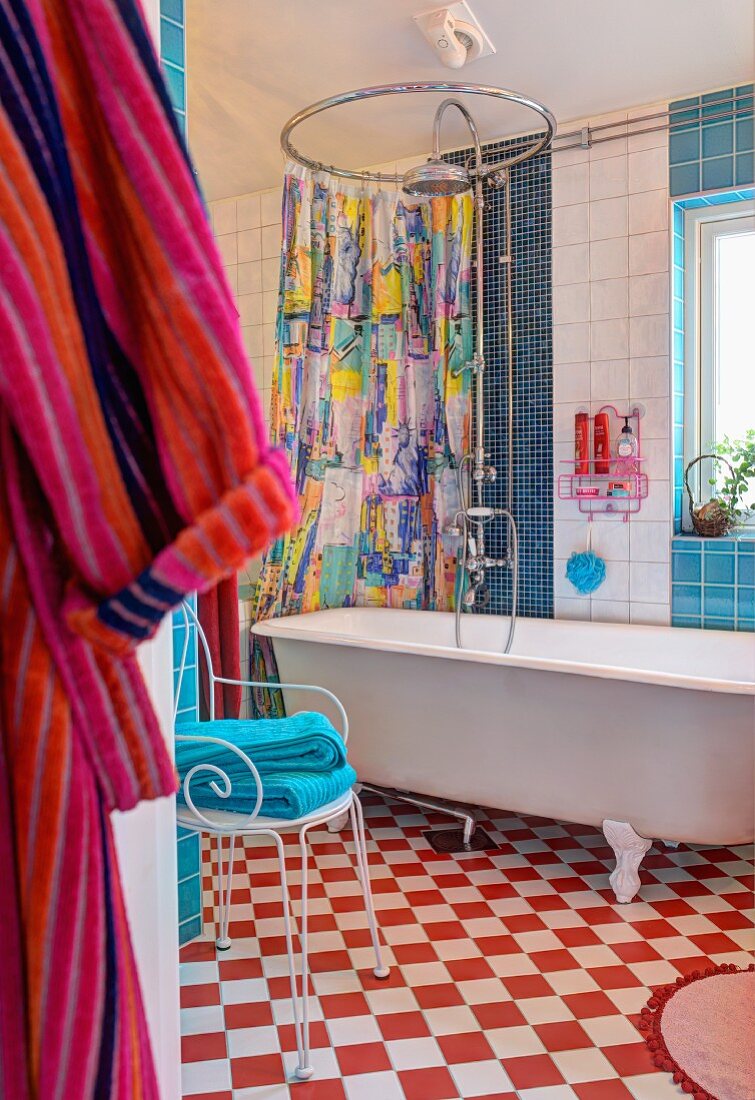 Badezimmer mit freistehender Badewanne auf rot-weißem Schachbrettmusterboden; Metallstuhl als Ablage