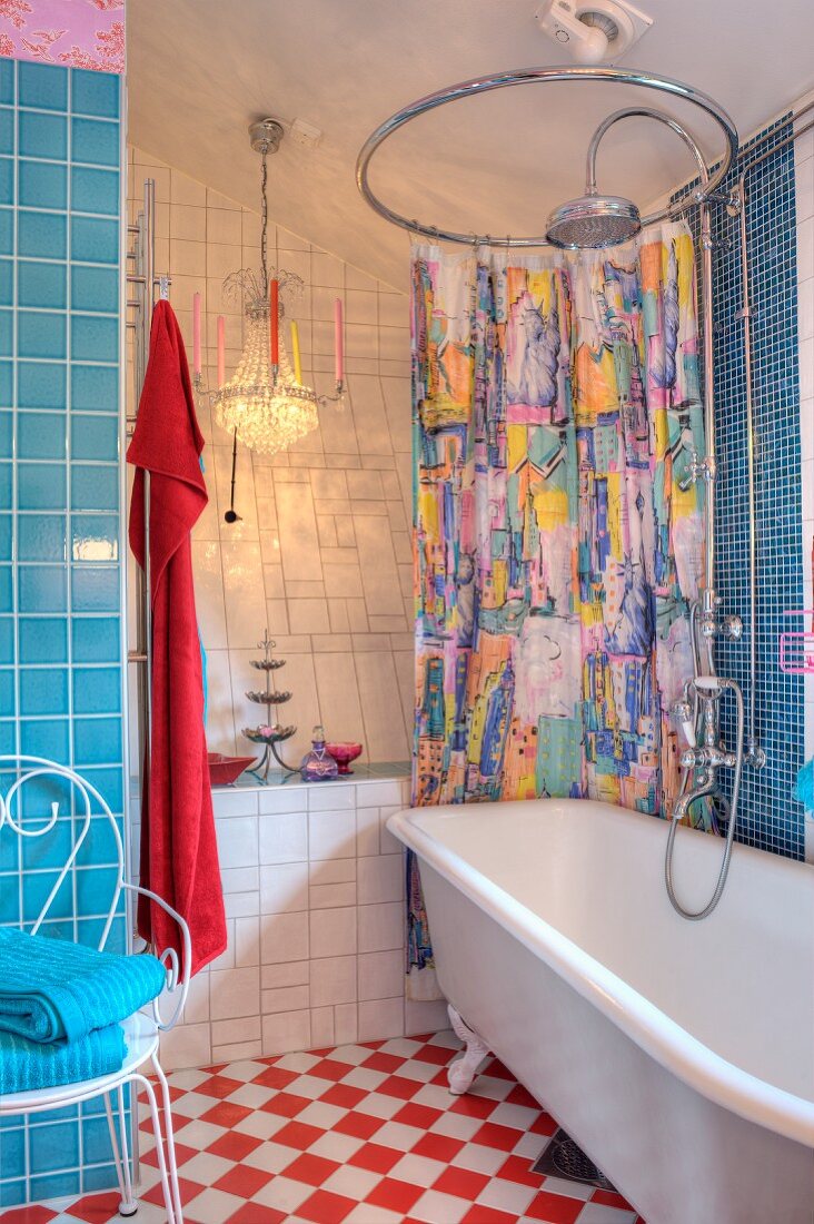 Bunter Duschvorhang mit runder Vorhangstange über Retro Wanne, dahinter Kronleuchter mit Kerzen und blau-weisser Fliesenmix