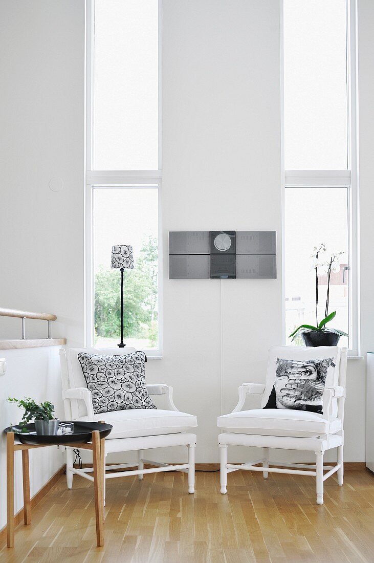 White armchairs and side table against wall with tall, narrow windows