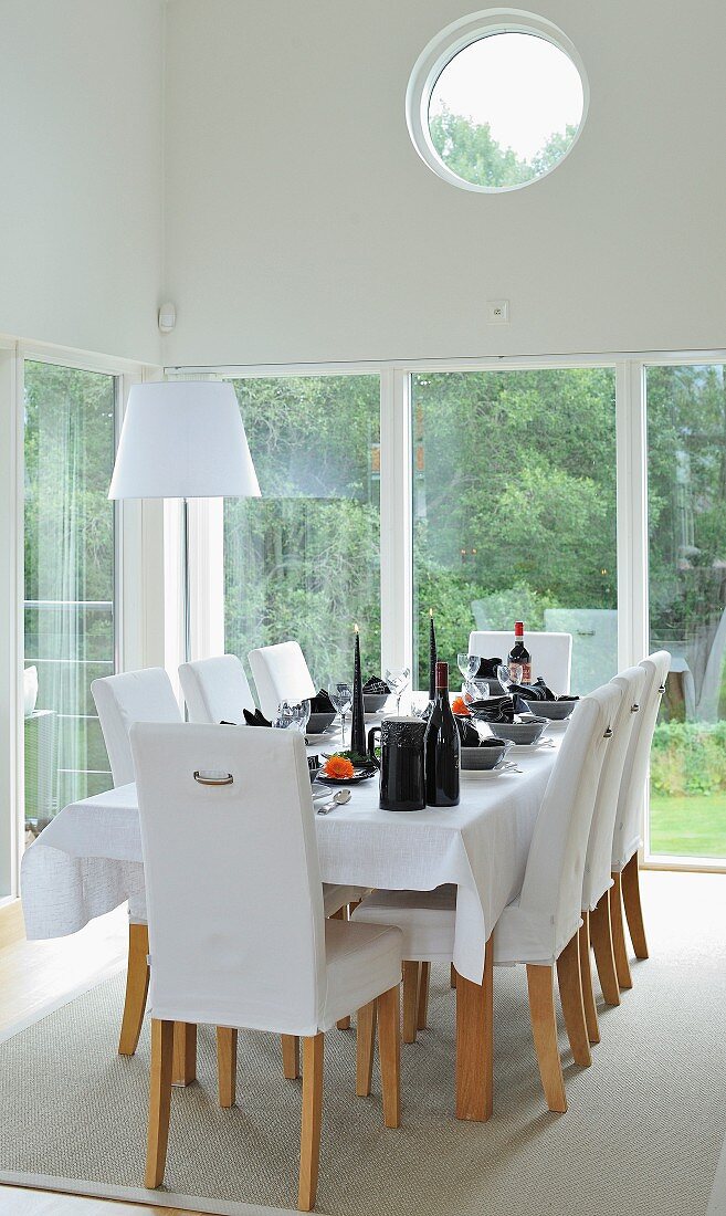 weiße, gepolsterte Stühle um festlich gedeckten Esstisch vor Fensterfront