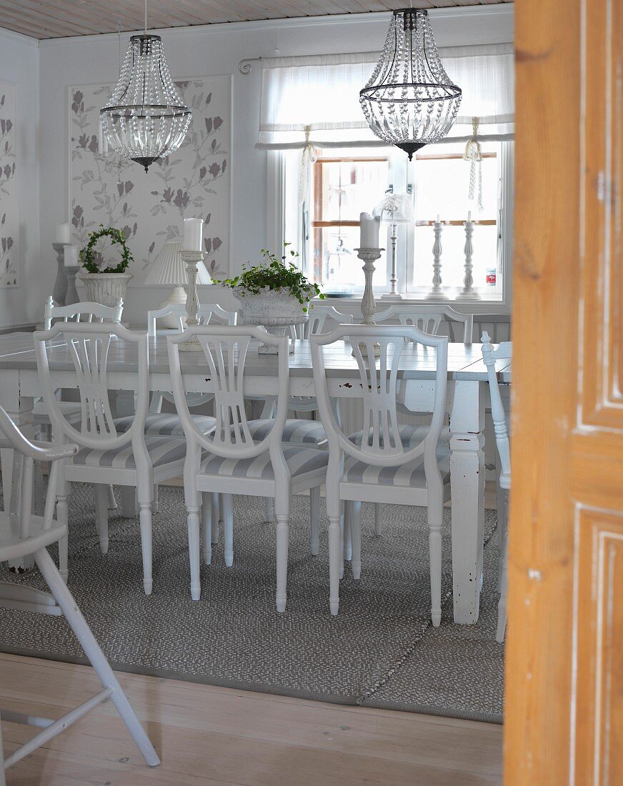 Blick durch offene Tür in Esszimmer mit weissen Holzstühlen um Tisch, darüber Kronleuchter mit Glasschmuck