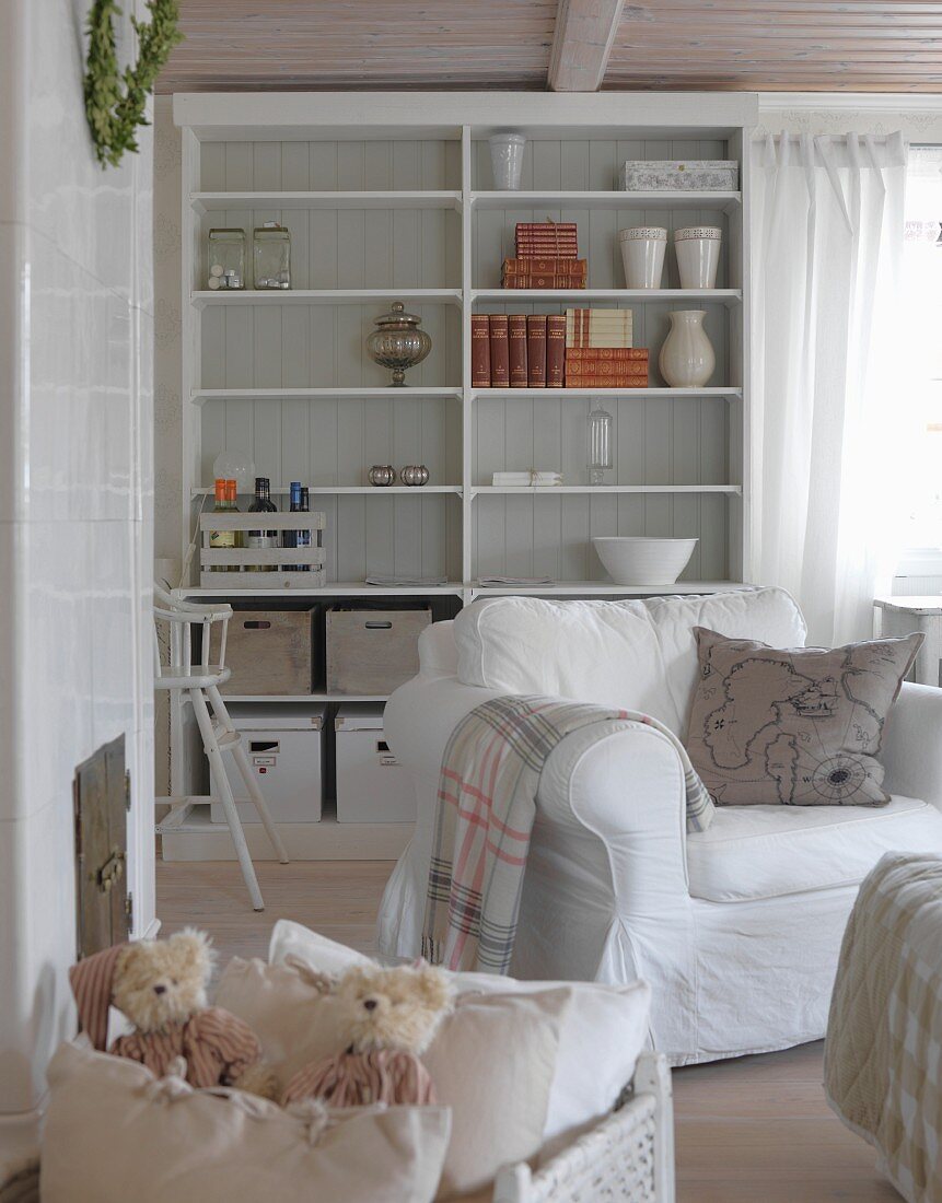White armchair in front of shelving with box of cushions and soft toys in foreground