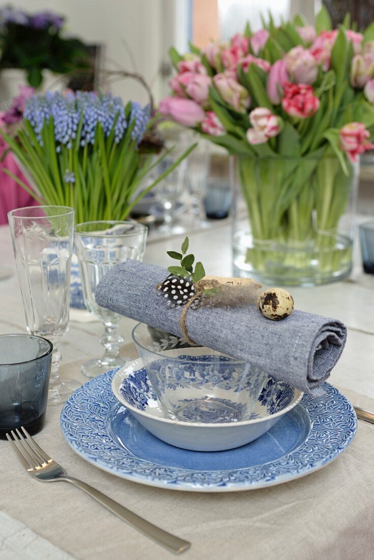 Gedeckter Tisch mit blau-weißem Geschirr, Serviette mit Wachtelei dekoriert, Traubenhyazinthen und Tulpen