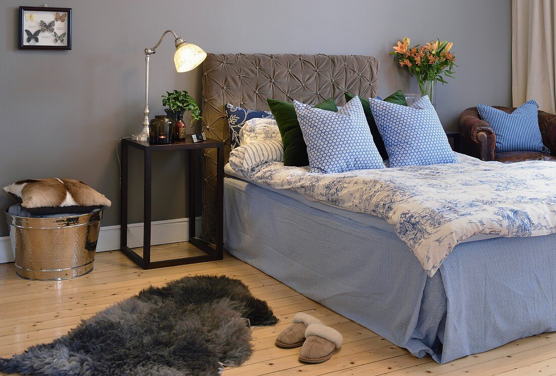 Bed with upholstered headboard and blue and white bed linen against grey-painted wall