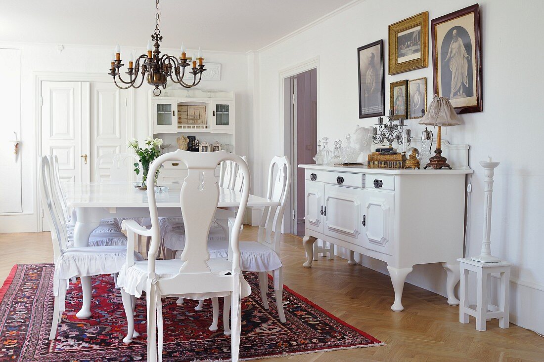 Antique, white, country-house-style dining set and sideboard against wall below gallery of pictures