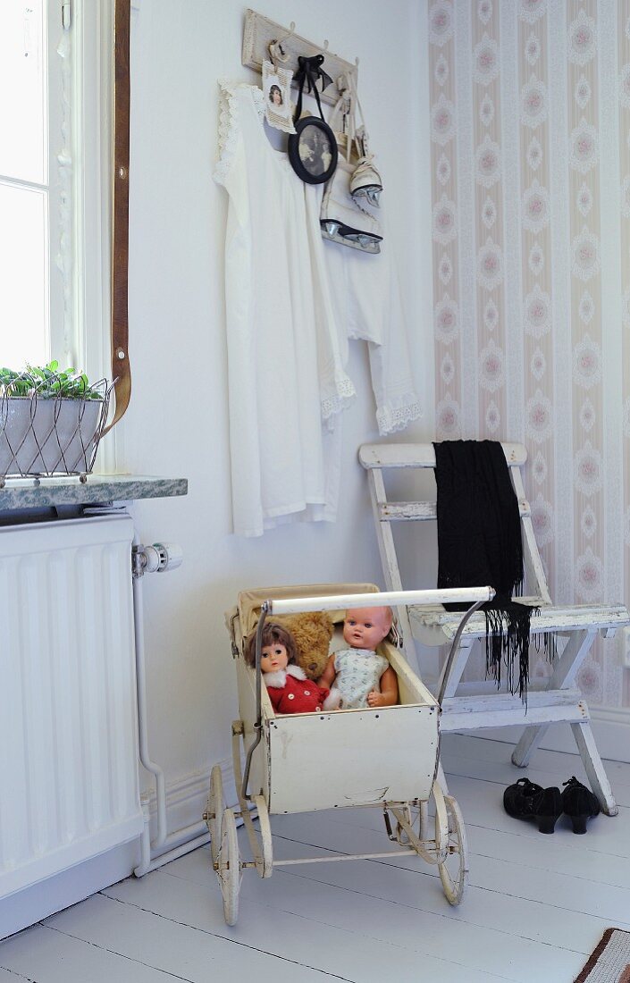 Vintage dolls' pram and white folding chair in corner of room with striped wallpaper