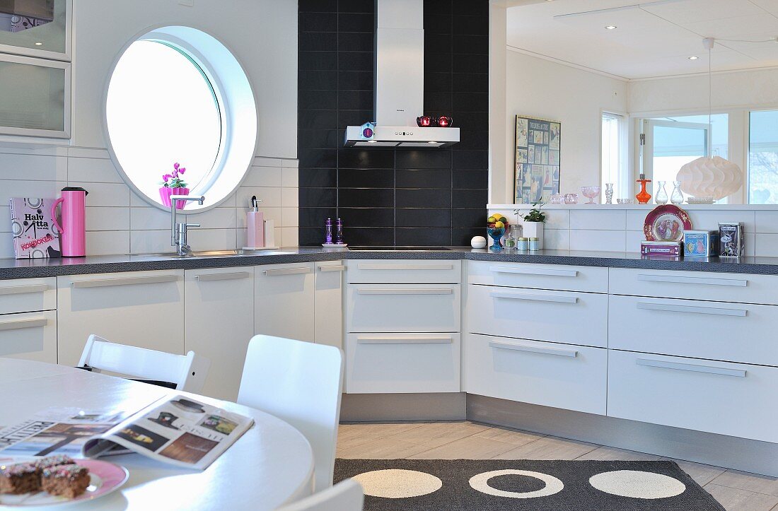 White kitchen counter with black wall tiles behind extractor hood next to porthole window