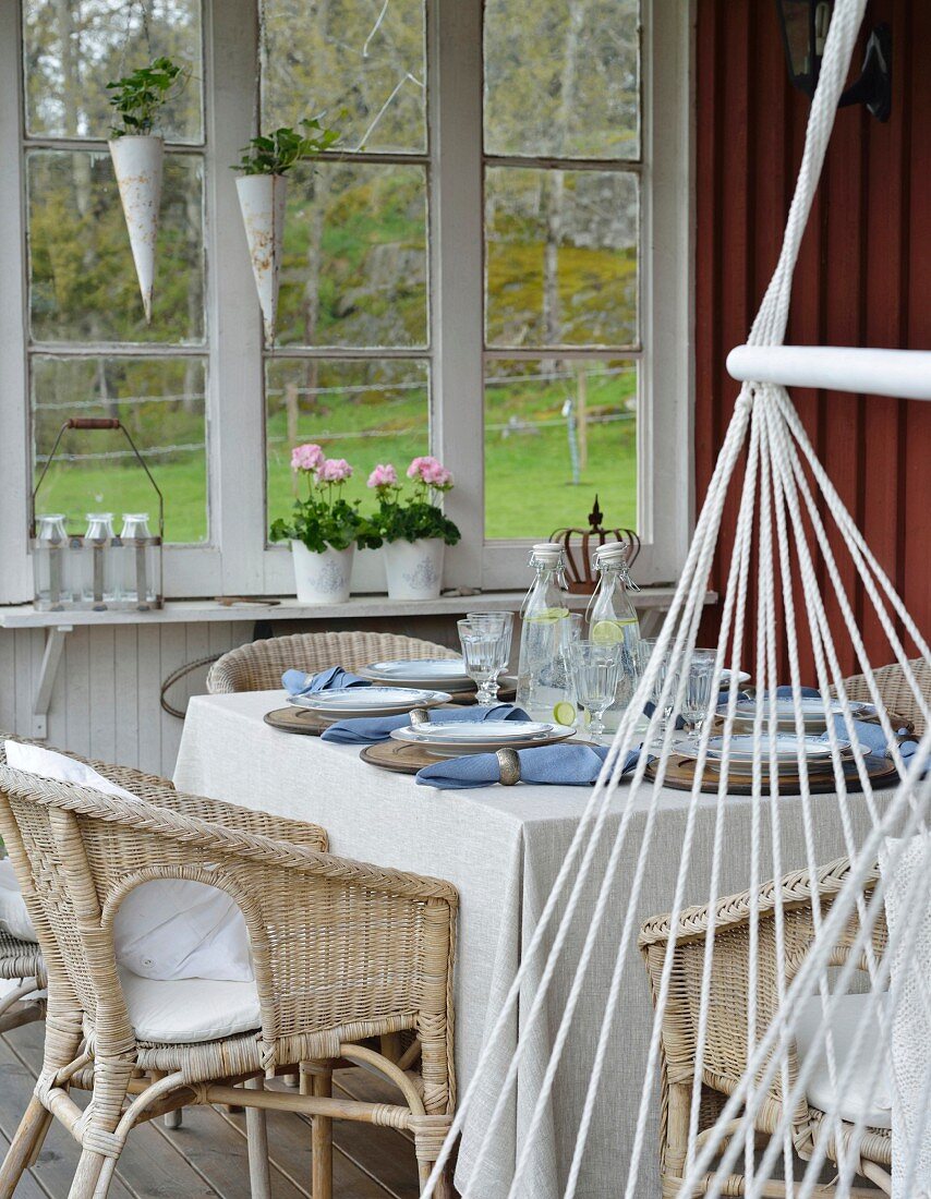 Wicker chairs at set table and hammock chair on wooden veranda