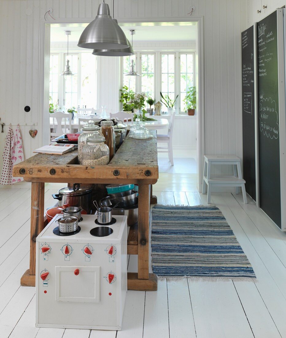 Toy cooker in front of old workbench used as kitchen counter in Scandinavian kitchen-dining room with white wooden floor