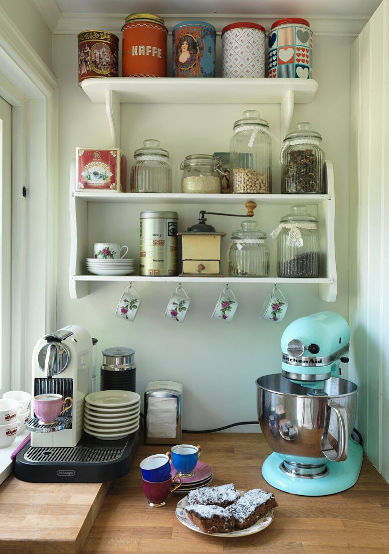 Retro Küchenmaschine und Espressomaschine auf Arbeitsplatte, darüber Wandbord mit Vorratsbehältern