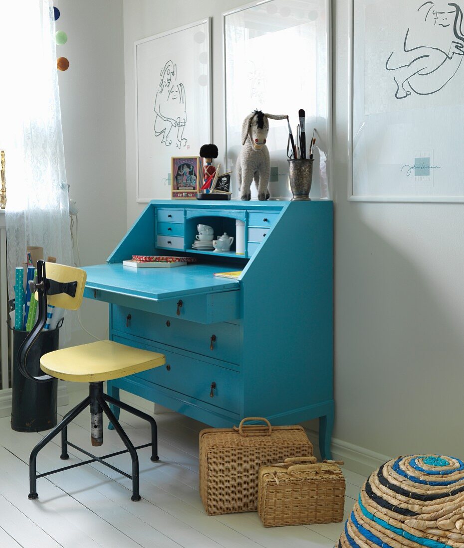 Vintage Drehstuhl vor blauem Sekretär, an Wand aufgehängte Zeichnungen mit weissen Rahmen