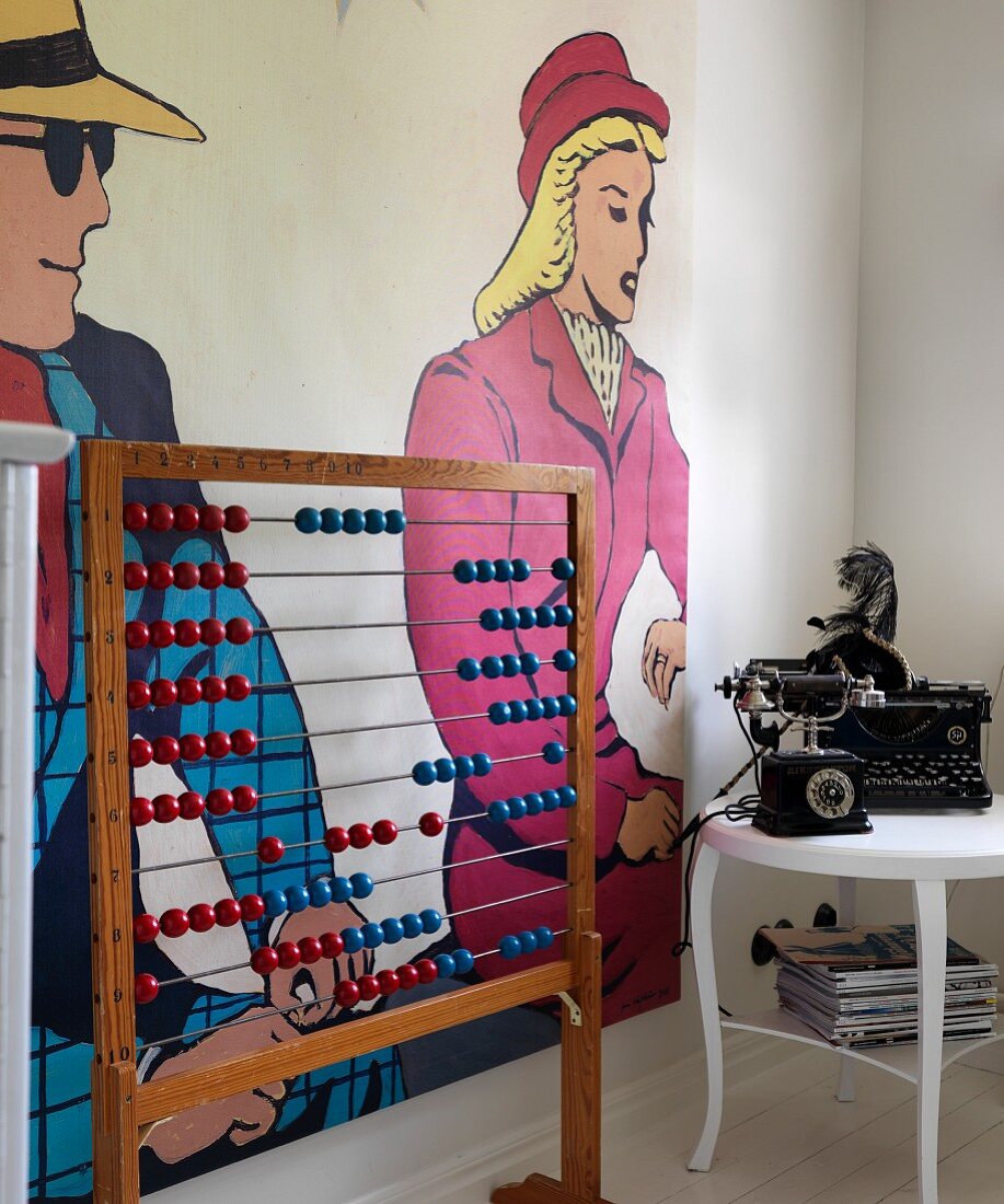Vintage Rechenschieber neben weißem Beistelltisch mit antikem Telefon und Schreibmaschine, an Wand Pop-Art-Kunst