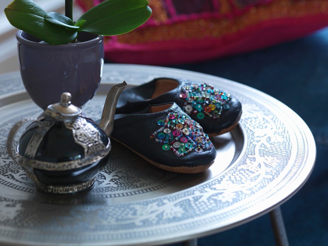 Mit Pailletten bestickte Lederpantoffeln und orientalische Teekanne auf marokkanischem Tabletttisch