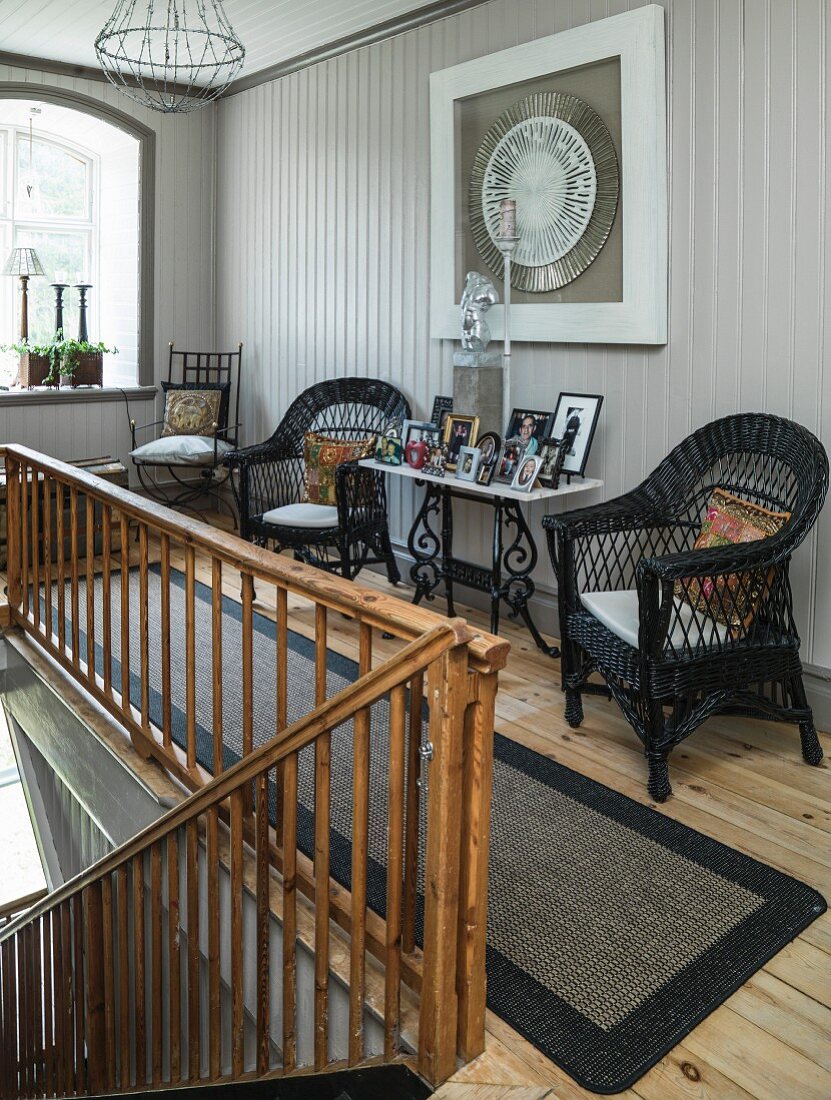 Schwarze Korbstühle und Konsolentisch mit Fotorahmen auf Treppenabsatz mit altem Holzgeländer