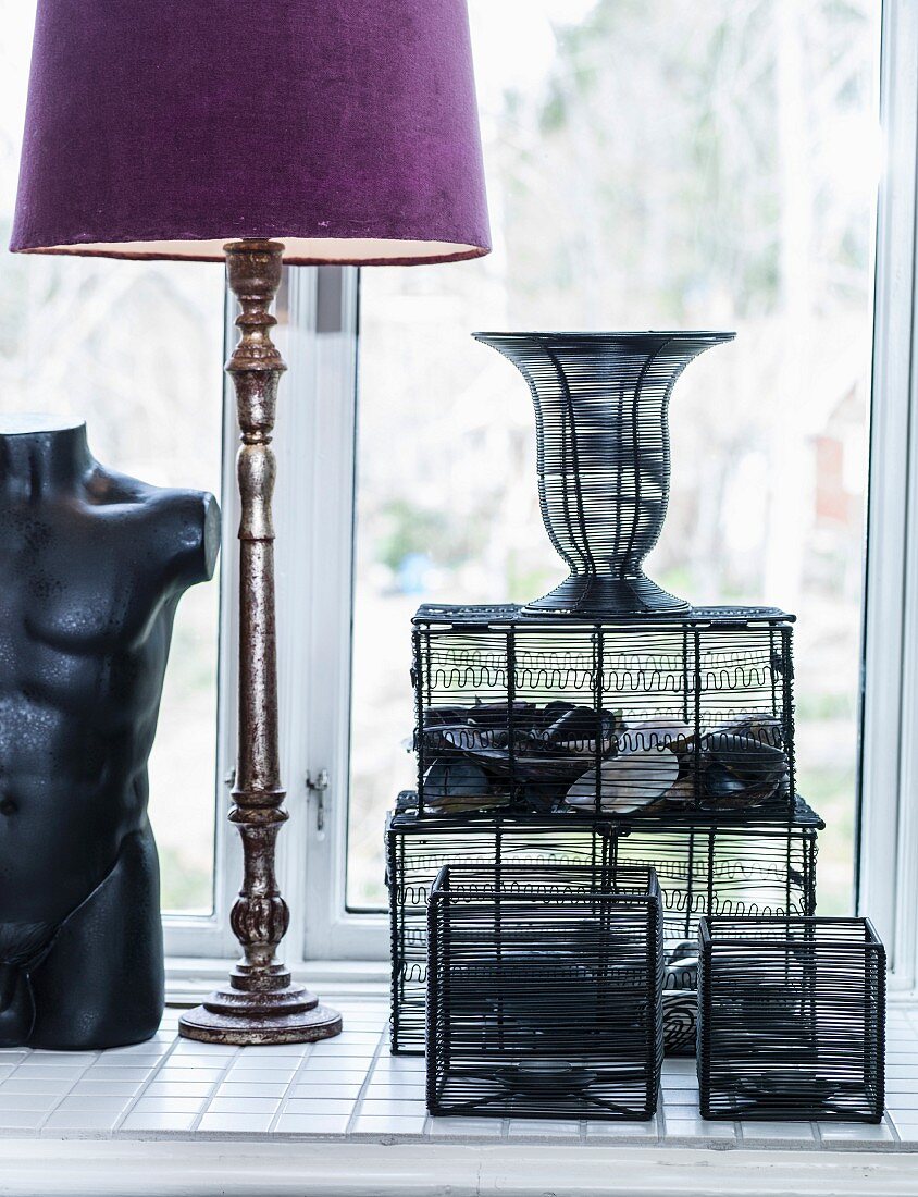 Still-life arrangement in window niche: wire baskets, table lamp and torso sculpture