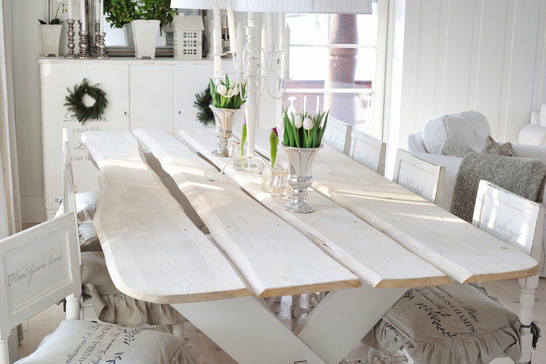 Weisses Shabby-Ambiente im Wohnraum eines skandinavischen Holzhauses mit rustikalem Esstisch und Typo-Print auf Stuhlkissen