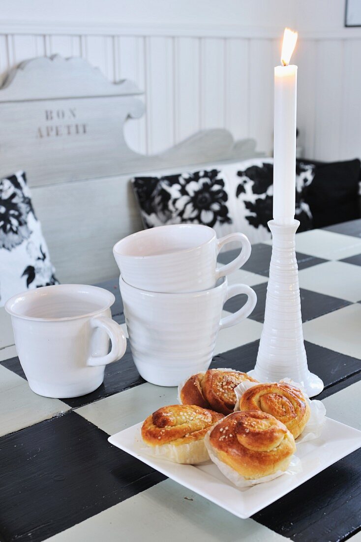Pastries, candles and cups on old dining table painted with black and white chequered pattern