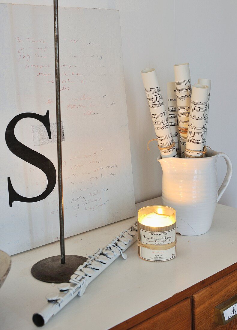 Rolled sheet music in ceramic jug, flute and vintage-style decorative letters on chest of drawers