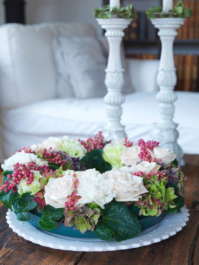 Tischkranz aus weissen Rosen und Beerenzweigen vor weissen Keramik Kerzenständer