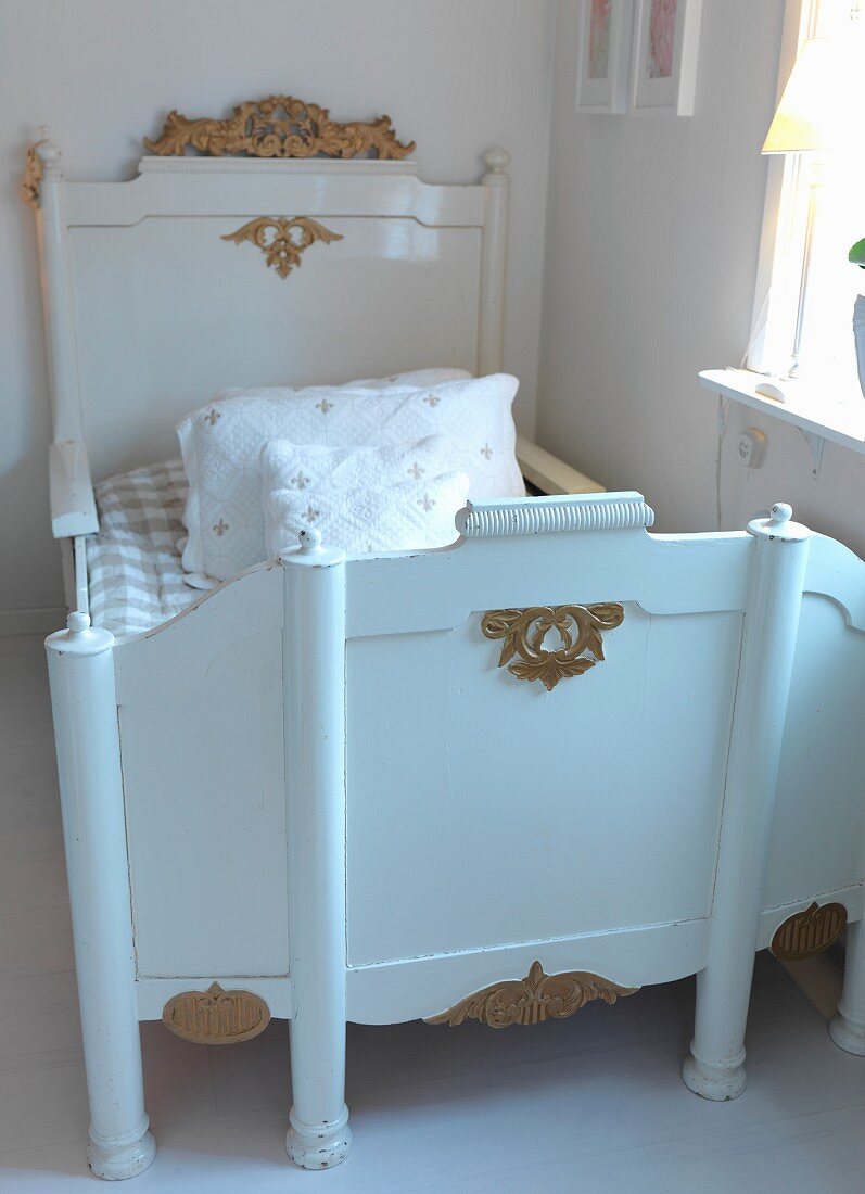 Antique child's bed painted white with gilt embellishments in corner of nursery