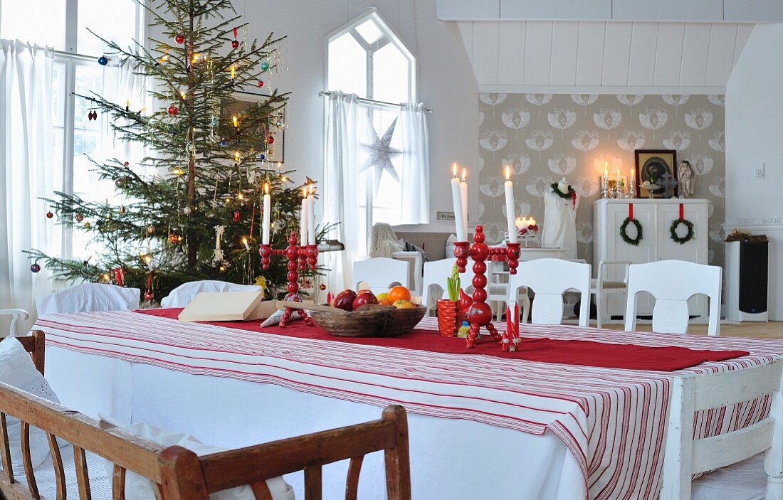 Red and white, Scandinavian arrangement on dining table in front of decorated Christmas tree