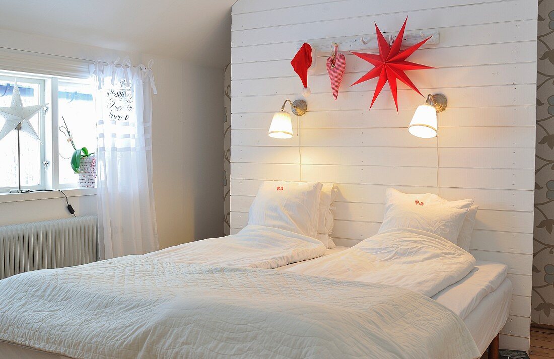 Schlafzimmer unterm Dach mit Stauraum hinter einer Rückwand mit Wandleuchten und roter Weihnachtsdeko