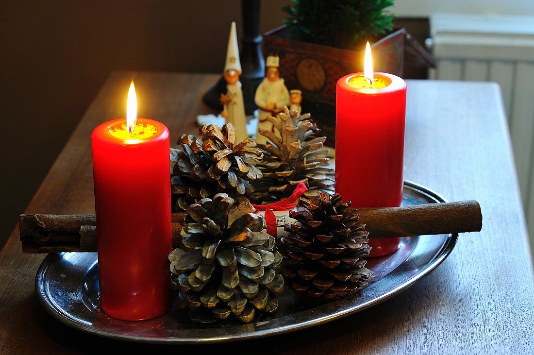Edelstahltablett mit brennenden Kerzen und Tannenzapfen auf einem Tisch, Dreikönigsfigürchen im Hintergrund