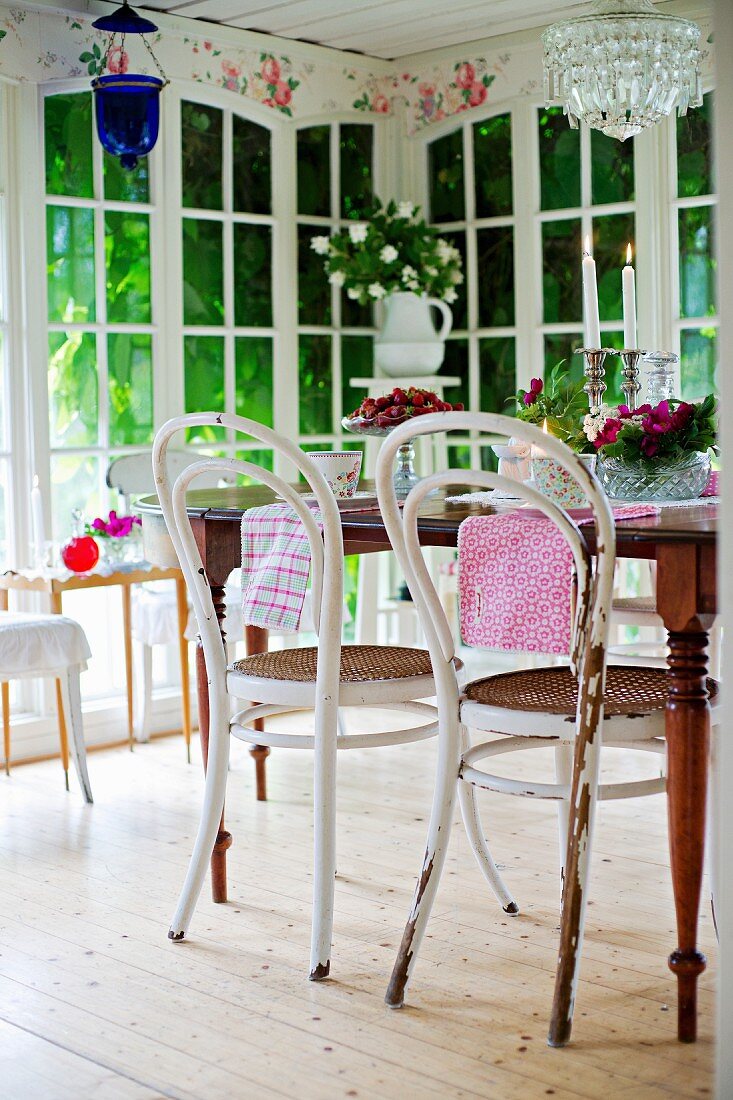 Thonetstühle mit weisser, abblätternder Farbe vor Tisch im Wintergarten, im Hintergrund raumhohe Sprossenfenster