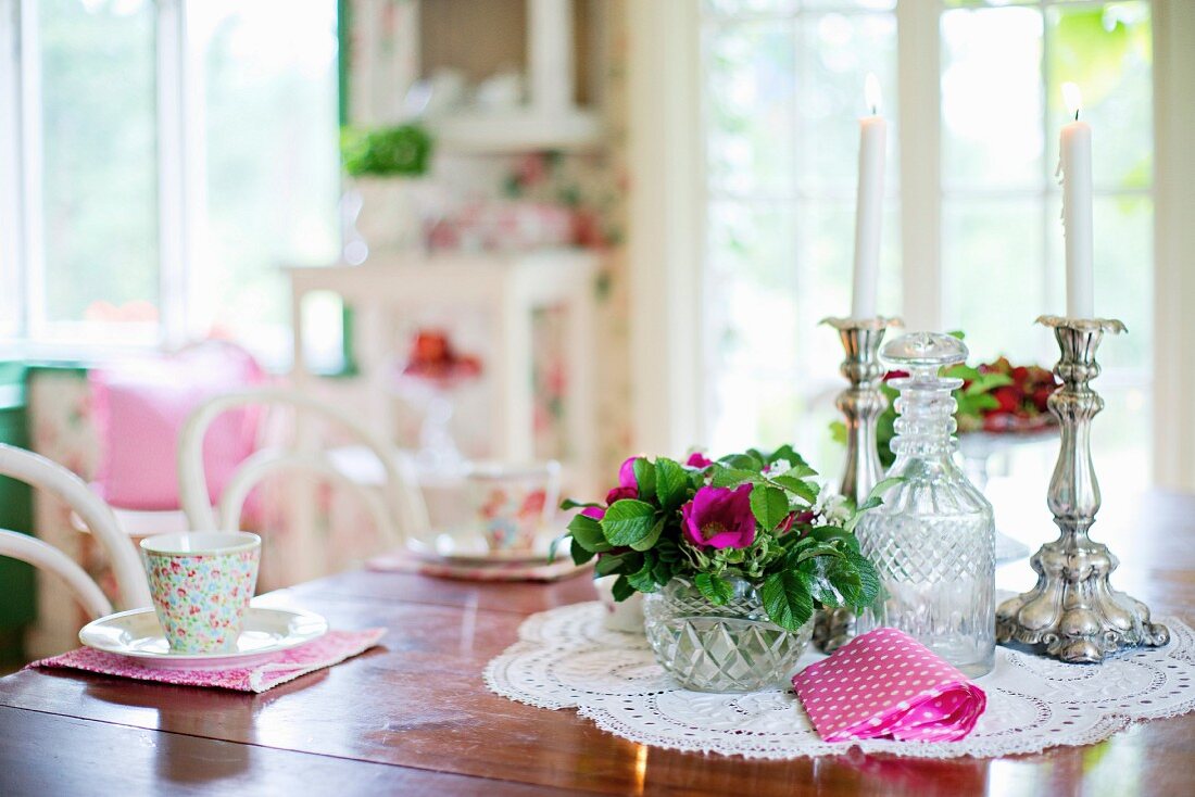 Esstisch mit Blumenschale, Kristallflasche und Kerzenhalter auf Spitzendeckchen